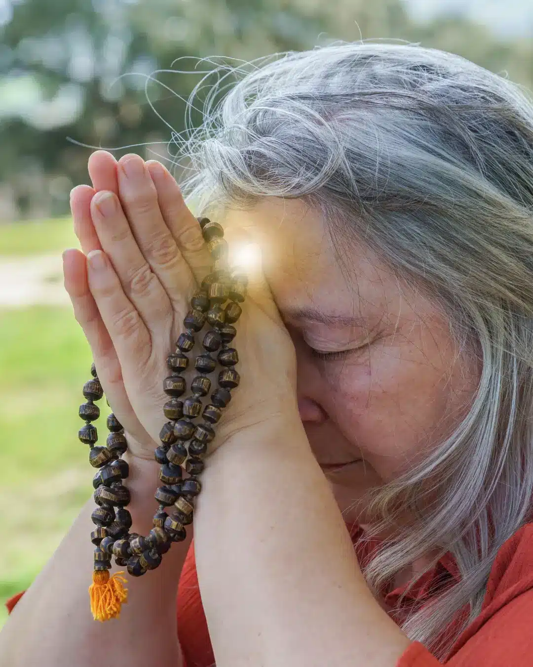 A mature woman with mala beads in prayer.
